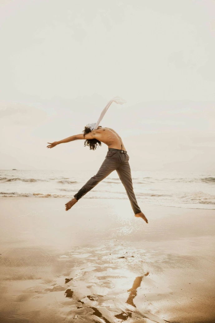 Person leaping mid-air over a wet sandy beach.